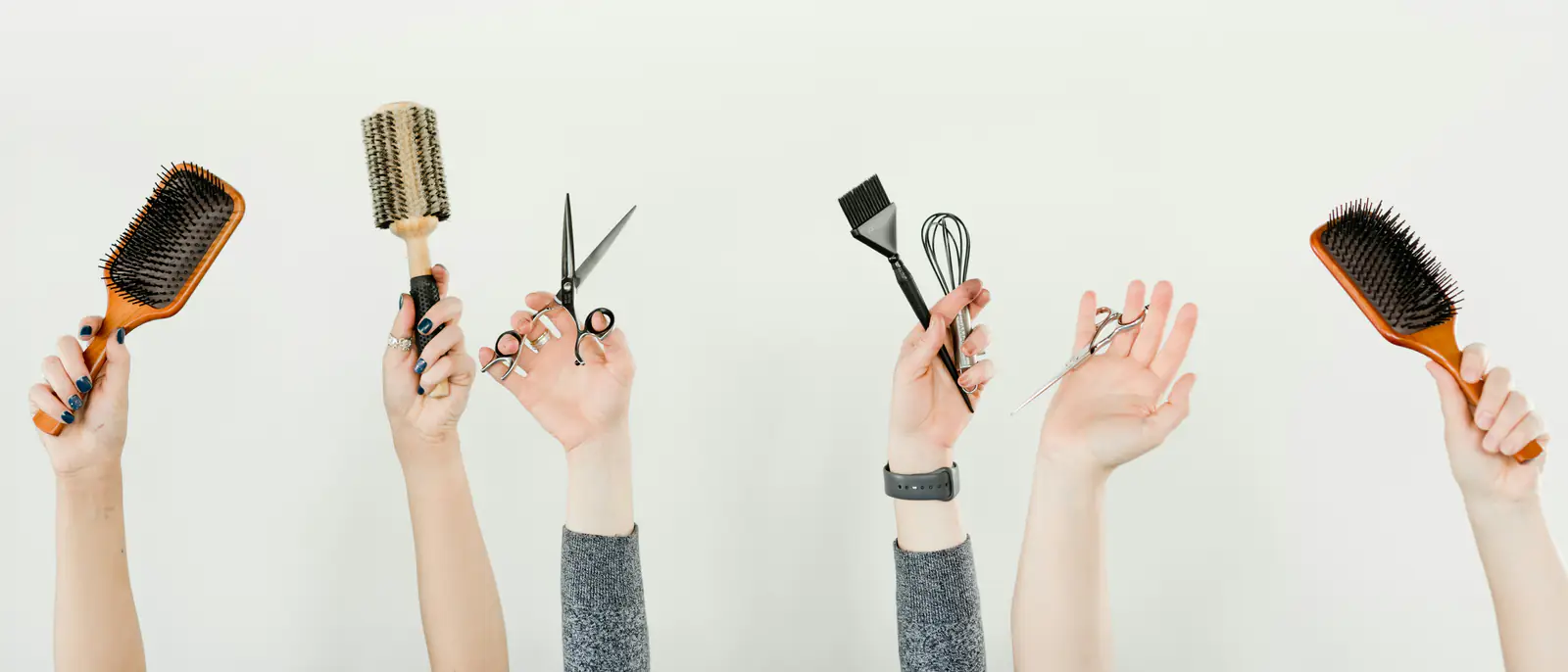 Des mains levées tenant brosses, ciseaux et pinceau à couleur