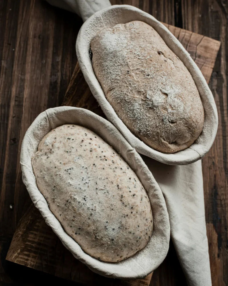 Deux pâtons au repos dans leurs bannetons farinés, sur une planche