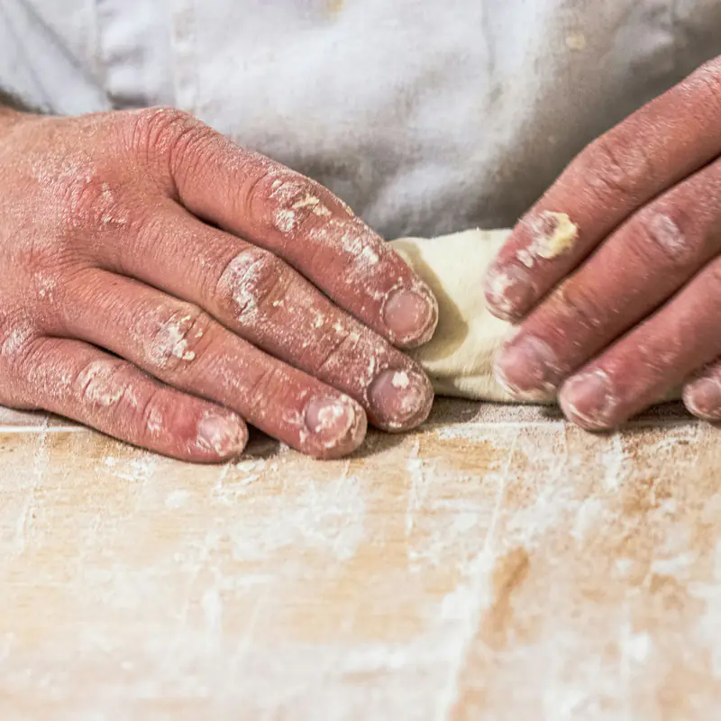 Des mains farinées façonnent un pâton sur le plan de travail