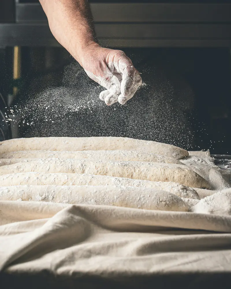 Le boulanger farine des baguettes façonnées posées sur la couche de lin