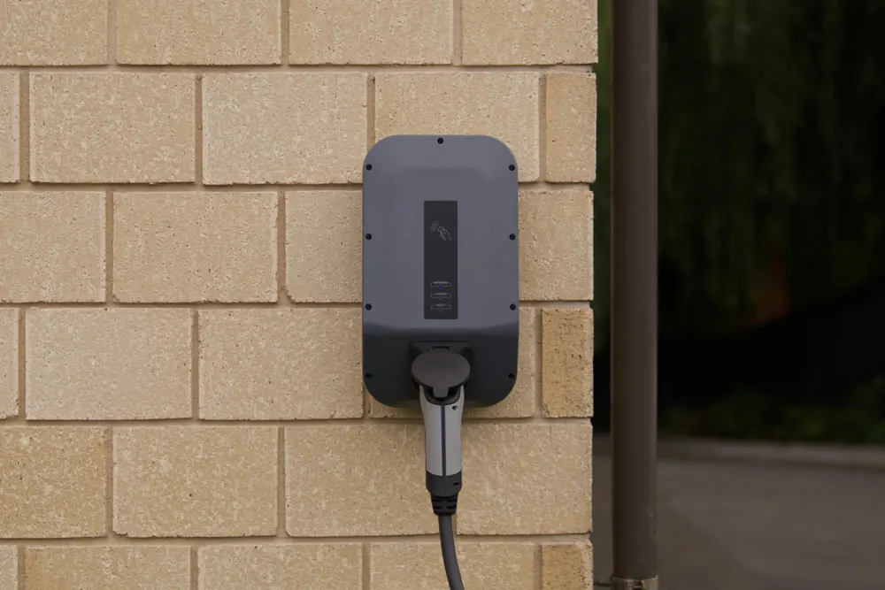 Une borne de recharge murale, son câble branché, sur un mur de briques claires