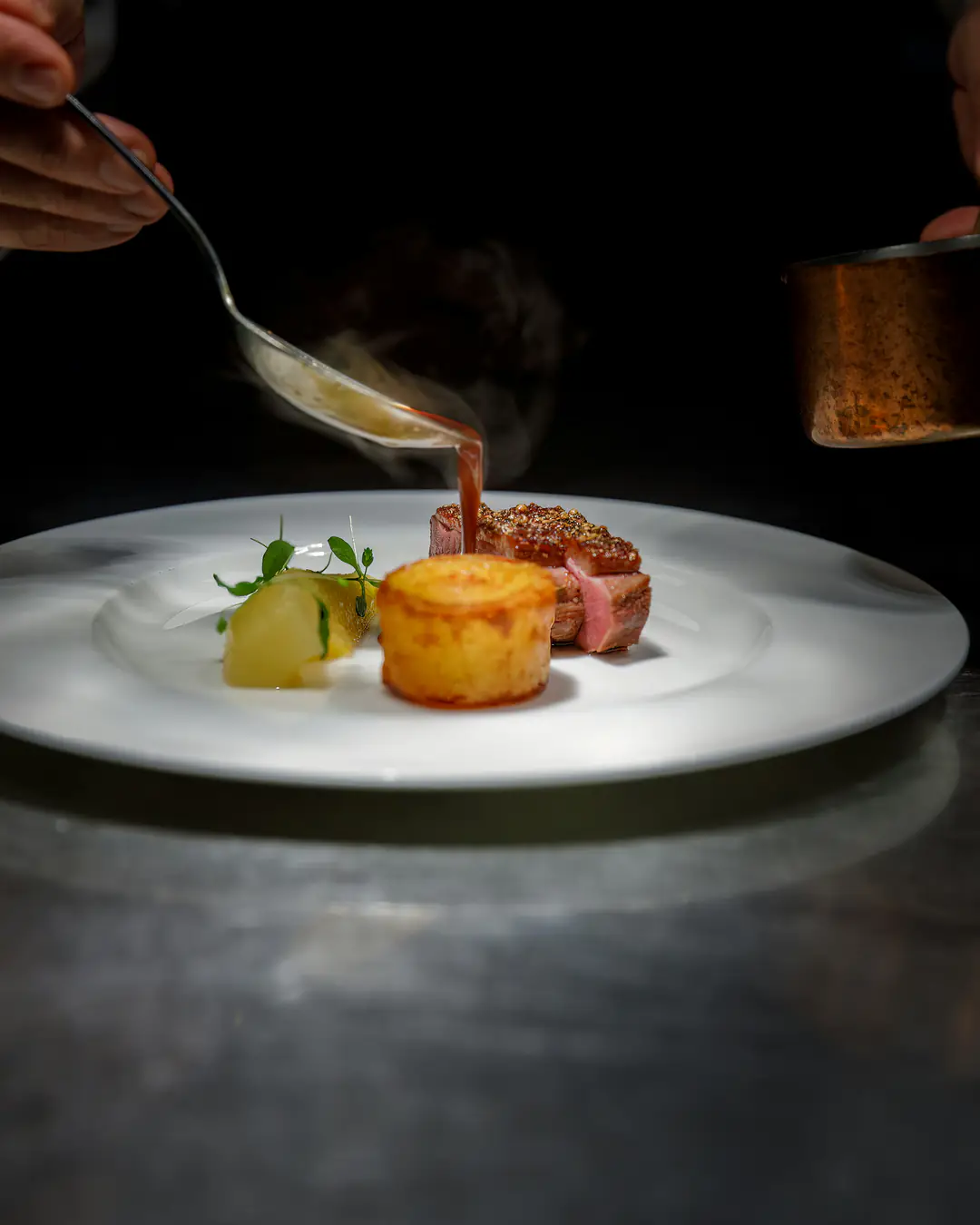 Une sauce versée à la cuillère sur une assiette, au moment de l’envoyer en salle