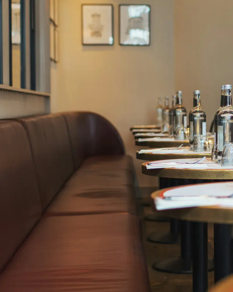 La salle, avec sa longue banquette de cuir face aux tables rondes dressées