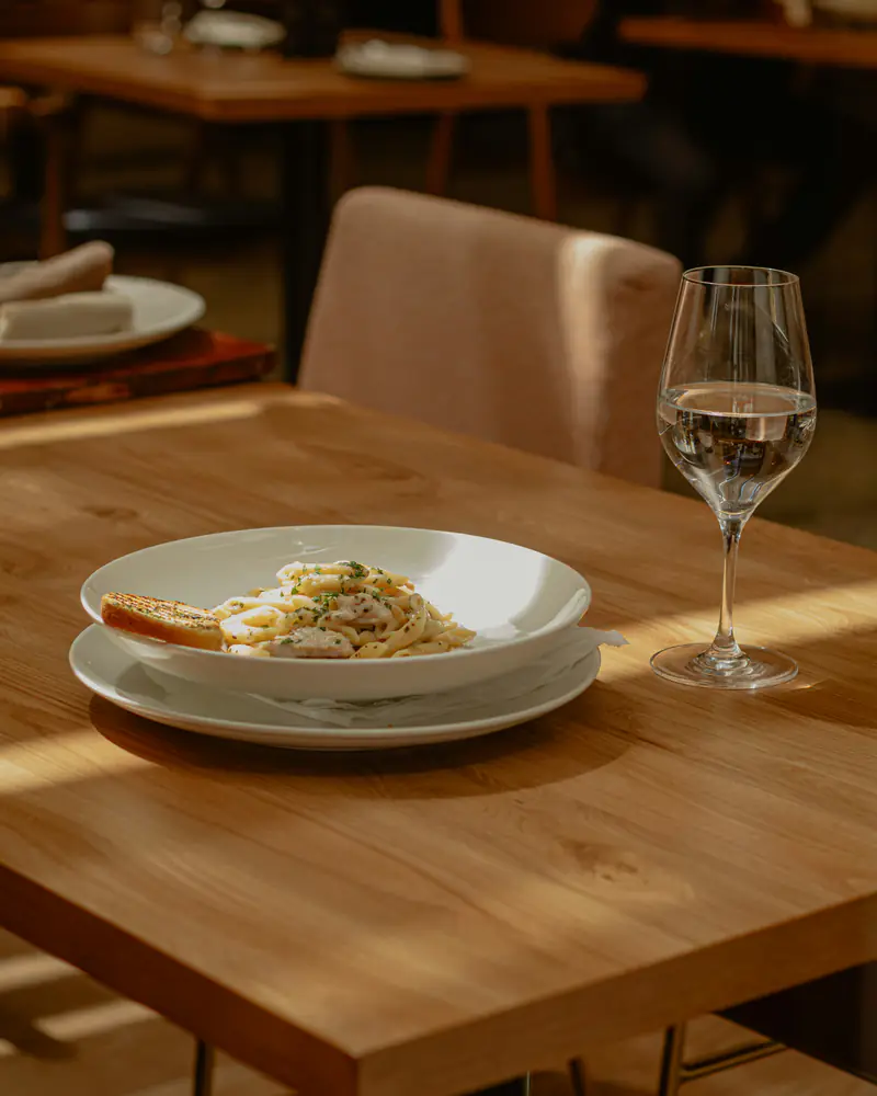 Une assiette et un verre sur une table en bois, dans la lumière de midi